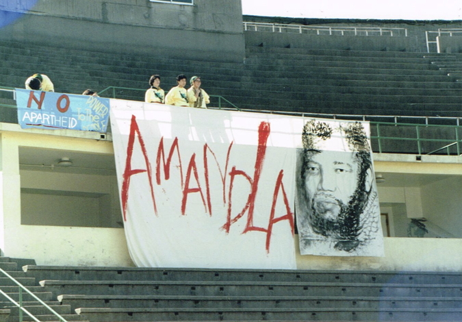 _ Volunteer organizers near a stage sign for “Amandla,” the South African cultural troupe in exile. Then touring in Japan, Amandla was scheduled to give a special show this day for the rally.  _ Volunteer organizers near a stage sign for “Amandla,” the South African cultural troupe in exile. Then touring in Japan, Amandla was scheduled to give a special show this day for the rally.
