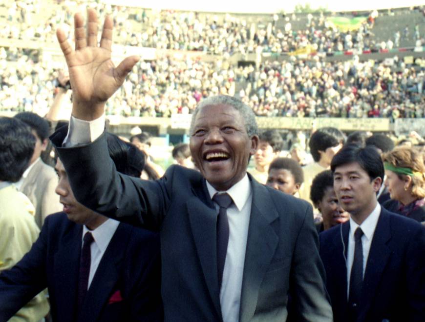 _ A last wave goodbye from Mandela, flanked by Japanese security police, as he departs the stadium for official meetings in Tokyo. [Kyodo News photo]